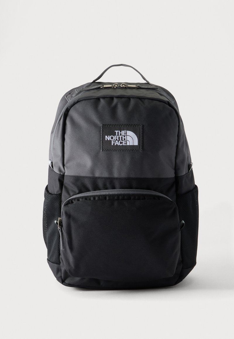 Zaino North Face nero e grigio scuro con tasca frontale con zip, tasche laterali in mesh e maniglia superiore su sfondo chiaro.