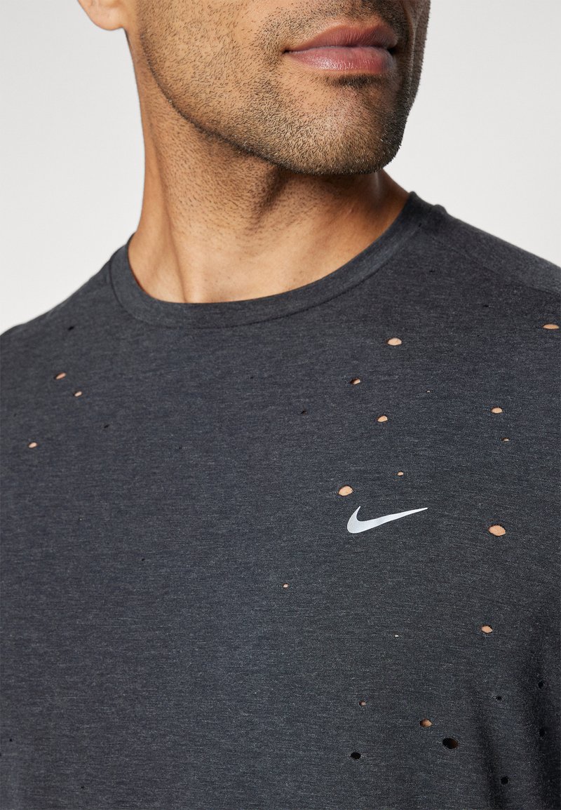 T-shirt grigio scuro con multiple lacerazioni, maniche corte e logo Nike bianco sul lato sinistro del petto. Tessuto in cotone.