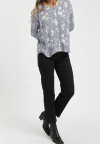 Blusa floreale grigia chiara con scollo a V, vestibilità ampia e maniche lunghe; abbinata a jeans neri a gamba dritta e stivaletti neri con tacco.
