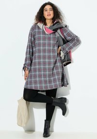 Abito a quadri grigio con dettagli in rosa e bianco, maniche lunghe e dettagli con cravatta. Abbinato a leggings neri e stivaletti; tiene una borsa tote beige.