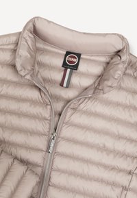 Veste matelassée beige clair avec col montant, fermeture éclair centrale et étiquette de la marque Colmar Originals à l'intérieur du col.