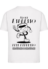 Valkoinen t-paita, jossa on musta sarjakuvamaista kahvikuppihahmoa juoksemassa, ja tekstinä "Enemmän espressoa, vähemmän depressoa" paksulla typografialla.
