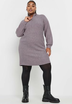 Lila, keskikokoinen mekko, jossa on korkea kaulus ja vetoketjukiinnitys, pitkät hihat ja pehmeä, tekstuuri. Mekko on yhdistetty mustiin nilkkasaappaisiin.