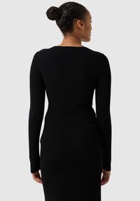 Zwarte ribbelige top met lange mouwen, een aansluitend ontwerp, ronde halslijn en een zachte textuur, gecombineerd met een gladde, zwarte, aansluitende rok.