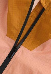 Lätt jacka med en rosa och orange färgblockdesign med rutmönster, svart dragkedja och slät finish vid kragen.