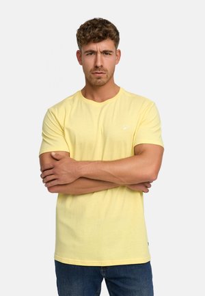 Gelbes Baumwoll-T-Shirt mit kurzen Ärmeln, Rundhalsausschnitt und kleinem weißen Logo auf der Brust. Getragen mit blauen Jeans.