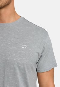 Graues Baumwoll-T-Shirt mit kurzen Ärmeln, Rundhalsausschnitt und subtiler Struktur. Verfügt über ein kleines Logo mit "EST. 1993" auf der Brust.