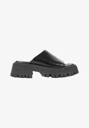 Czarne buty typu mule na wsuwkę z grubą, masywną, żebrowaną podeszwą oraz gładką, szeroką skórzaną cholewką zakrywającą palce, pokazane z boku na białym tle.