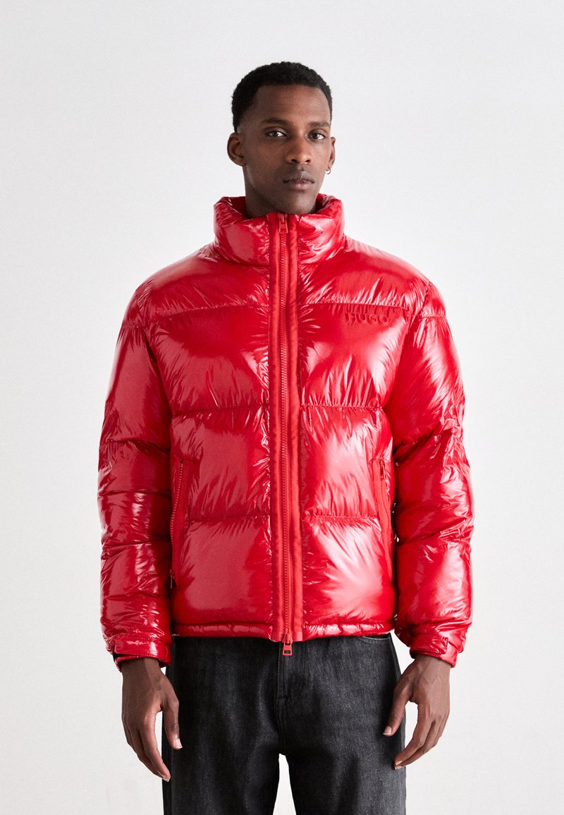 Red puffer jacket with a glossy finish, high collar, and zip closure. Features padded sections and side pockets.