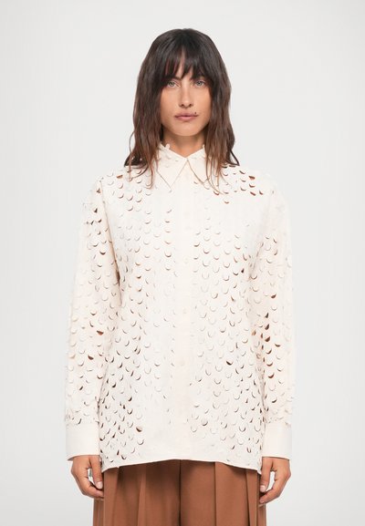 Chemise blanche à manches longues avec un motif découpé intégral et fermeture par bouton. Le tissu a une texture lisse avec une coupe décontractée.