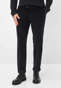 Zwarte corduroybroeken met een slim fit, voorzien van een knoopsluiting, zijzakken en opgerolde boorden, gecombineerd met zwarte leren laarzen.