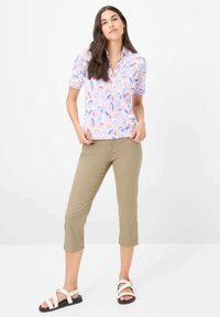 Polo a maniche corte di colore viola chiaro con motivo a foglie multicolori, abbinato a pantaloni culotte beige e sandali bianchi con suola nera.