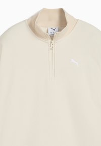 Cremfarbener Pullover mit einem Halsreißverschluss, strukturiertem Material und einem weißen Puma-Logo auf der Brust. Leichtes und lässiges Design.