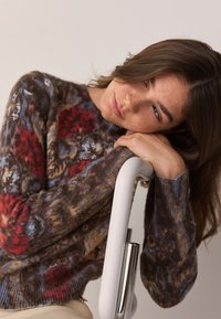 Višenamjenski džemper s cvjetnim uzorkom u nijansama smeđe, crvene i plave boje. Rebrasti rubovi na rukavima i okrugli izrez. Mekani, teksturirani materijal.