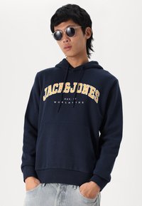 Navyblauwe hoodie van een katoenmix, met "JACK&JONES" in vetgele letters en een kangoeroezak. Voorzien van een trekkoord.