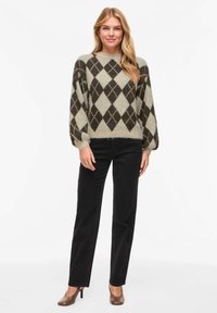 Pull en tricot avec une base grise et un motif argyle marron foncé et crème, col rond, manches ballon, associé à un pantalon noir.