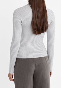 Jasnoszara prążkowana dzianinowa bluzka z długim rękawem o dopasowanym kroju, z wysokim kołnierzem i teksturowaną tkaniną. Noszona z ciemnoszarymi spodniami.