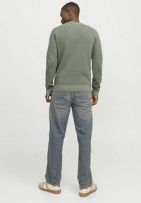 Grüner Strickpullover mit strukturiertem Stoff, Rundhalsausschnitt und gerippten Bündchen, kombiniert mit hellblauen Jeans und beigen Schuhen.