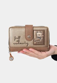 Billetera de metal dorado con acabado texturizado, cierre de cremallera y acentos marrones. Presenta un diseño de gato y la frase "lleno de curiosidad".