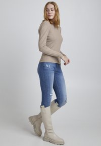 Beige ribbad långärmad topp som kombineras med slitna blå skinnyjeans och beiga knähöga stövlar med tjock sula.