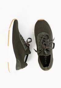 Olivgrüne Sportschuhe mit atmungsaktivem Mesh-Obermaterial, Schnürverschluss, Zuglasche und weißer Sohle mit hellbraunen Akzenten.
