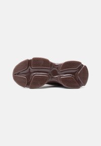 Sole di sneaker marrone con battistrada in gomma segmentata e motivi a zigzag su uno sfondo bianco puro.