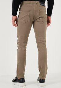 KHAKI uske slim-fit hlače od glatke mješavine pamuka, s dva stražnja džepa, u kombinaciji s crnim tenisicama.