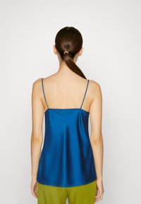 Syväsininen satiininen camisole, jossa on ohut olkaimet, takasauma ja väljä malli, yhdistetty vihreisiin housuihin. Sujuva, kiiltävä rakenne.