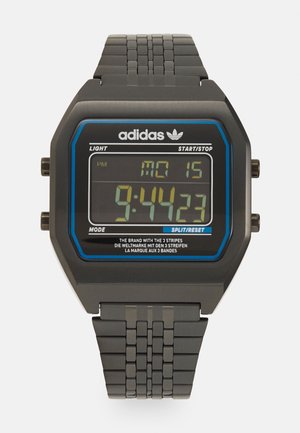 Montre numérique noire avec un cadran rectangulaire, des accents bleus et un bracelet texturé. L'affichage montre l'heure, la date, et des boutons sur le côté pour les fonctions.