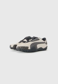 Light beige and dark gray Puma sneakers with textured soles and crisscross elastic straps, displayed on a plain white background.