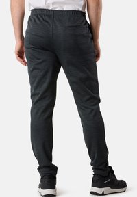 Dunkelgraue Jogginghosen aus einem weichen, strukturierten Stoff mit einem elastischen Bund und einer Reißverschlusstasche auf der Rückseite. Getragen mit schwarzen Sportschuhen.