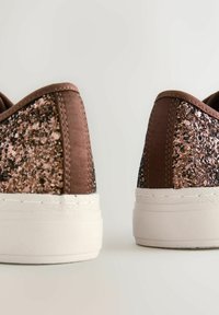 Adidași maro cu un panou texturat din glitter pe toc, tălpi din cauciuc alb și un superior din textil neted cu cusături contrastante.