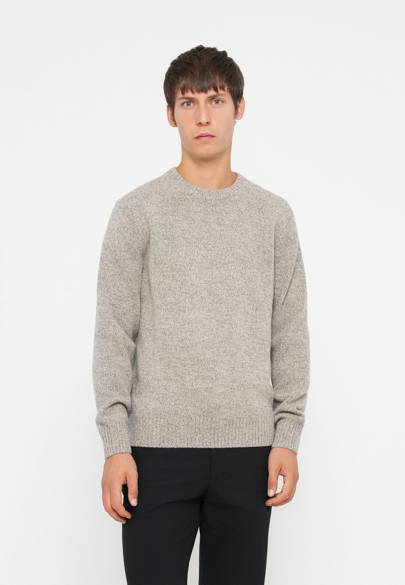 Light gray knit sweater with a round neckline, ribbed cuffs, and hem. Smooth texture and loose fit, worn with dark trousers.