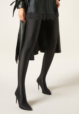 Collant neri opachi con finitura satinata, con un delicato bordino in pizzo in vita. Abbinati a décolleté nere a punta con tacco a stiletto.