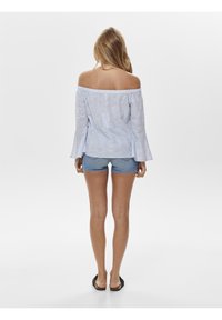 Top azzurro chiaro a spalle scoperte con motivo ad occhio di pernice, maniche a campana e vestibilità ampia. Abbinato a pantaloni shorts in denim e sandali neri.