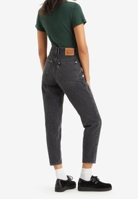 Högmidjade svarta jeans, rak benklippning, med bakfickor och en märkesläderpatch. Bärs med en grön T-shirt och svarta skor.