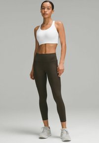 Top corto blanco con tirantes anchos combinado con leggings de cintura alta color verde oliva. Tela texturizada, diseño ajustado y zapatillas deportivas.
