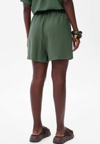 Zielone, krótkie, luźne spodenki z elastycznym pasem. Teksturowana tkanina, w komplecie z brązowymi klapkami na płaskiej podeszwie.