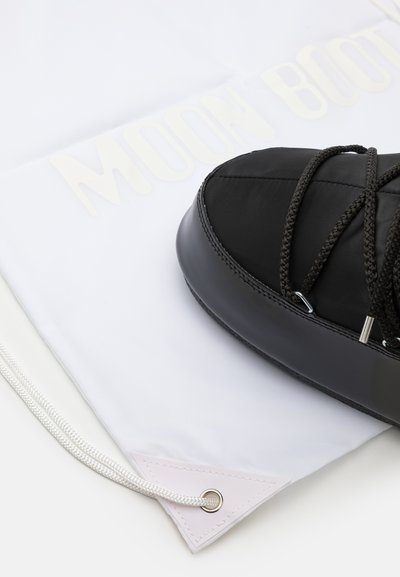 Bottine noire imperméable avec un dessus texturé, semelle épaisse et lacets noirs, posée sur un sac à cordon blanc portant le texte "MOON BOOT".