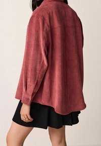 Czerwona koszula z sztruksu z długimi rękawami i kołnierzykiem, cechująca się luźnym krojem oraz mankietami zapinanymi na guziki, zestawiona z czarną spódnicą.