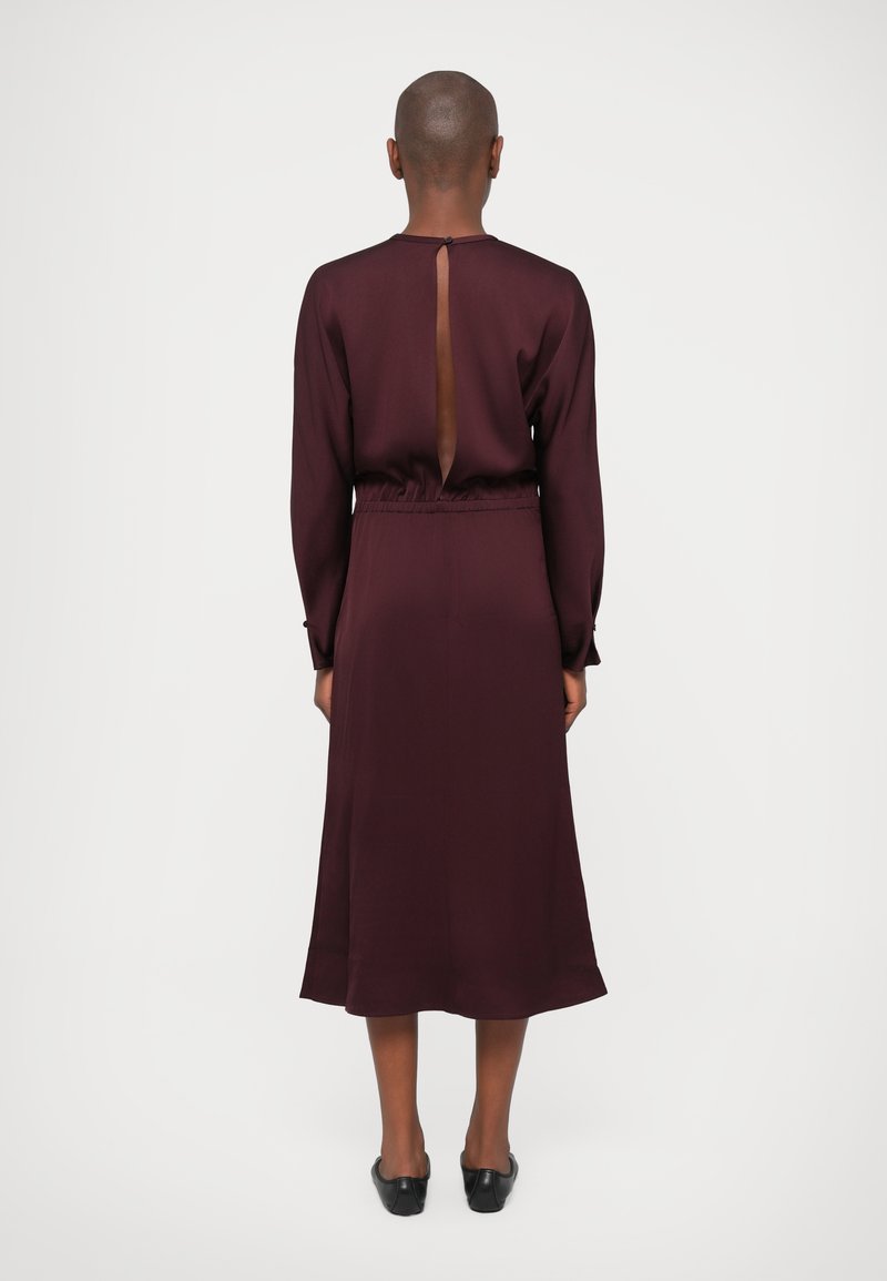 Burgunderrotes Langarmkleid mit einem Rückenschlitz, elastischem Bund und fließendem Saum. Glatte Stoffoberfläche mit matter Textur.