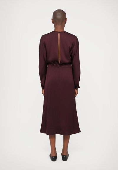 Rochie lungă burgundă cu mâneci lungi, decolteu la spate, talie elastică și tiv fluid. Material neted cu textură mată.
