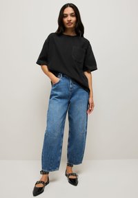 T-shirt en coton noir oversize avec une poche poitrine, associé à un pantalon en jean bleu clair taille haute et des ballerines noires à bouts pointus.