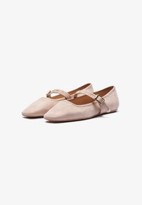 Ballerine a punta in suede beige chiaro con una sottile cinghia alla caviglia e una fibbia dorata. Texture liscia e design minimalista.