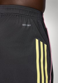 Svarte treningsshorts med teksturert overflate, som har et gult stripe mønster og et rosa accent. Inkluderer "AEROREADY" logo på livlinningen.