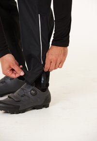 Zwarte fietsbroek met een zijrits en klittenbandsluiting, gecombineerd met gestructureerde zwarte fietsschoenen met een draaisysteem voor aanpassing.