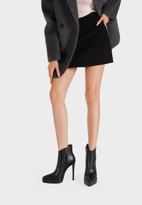 Stivaletti in pelle nera con tacco a stiletto alto, punta arrotondata e zip laterale. Texture liscia e design elegante, ideali per abbigliamento formale.