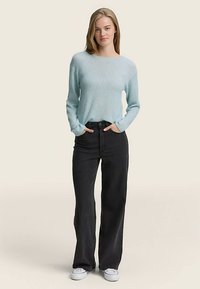 Svetlo modra pletena majica z dolgimi rokavi in okroglim izrezom, nošena preko črnih širokih kavbojk in belih superg. Mehka tekstura, sproščen kroj.