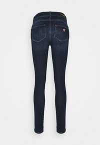 Jeans ajustados en denim azul oscuro. Cuentan con una cintura alta, dos bolsillos traseros y una sutil etiqueta de marca en la parte trasera. Textura suave.