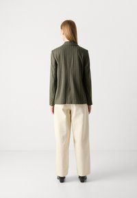 Olive rohelise triibuga bleiser rõhuga sobivusele, ühe avaga ja dekoratiivsete nööbiga detailidega, koos kreemivärvi laia säärega pükstega.